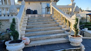 Een stenen trap die leidt naar een gebouw met een pannendak, aan weerszijden omlijst door decoratieve balustrades en potplanten.