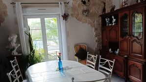 Een eetgedeelte met een ronde tafel, witte stoelen, een blauwe vaas en een stenen muur.