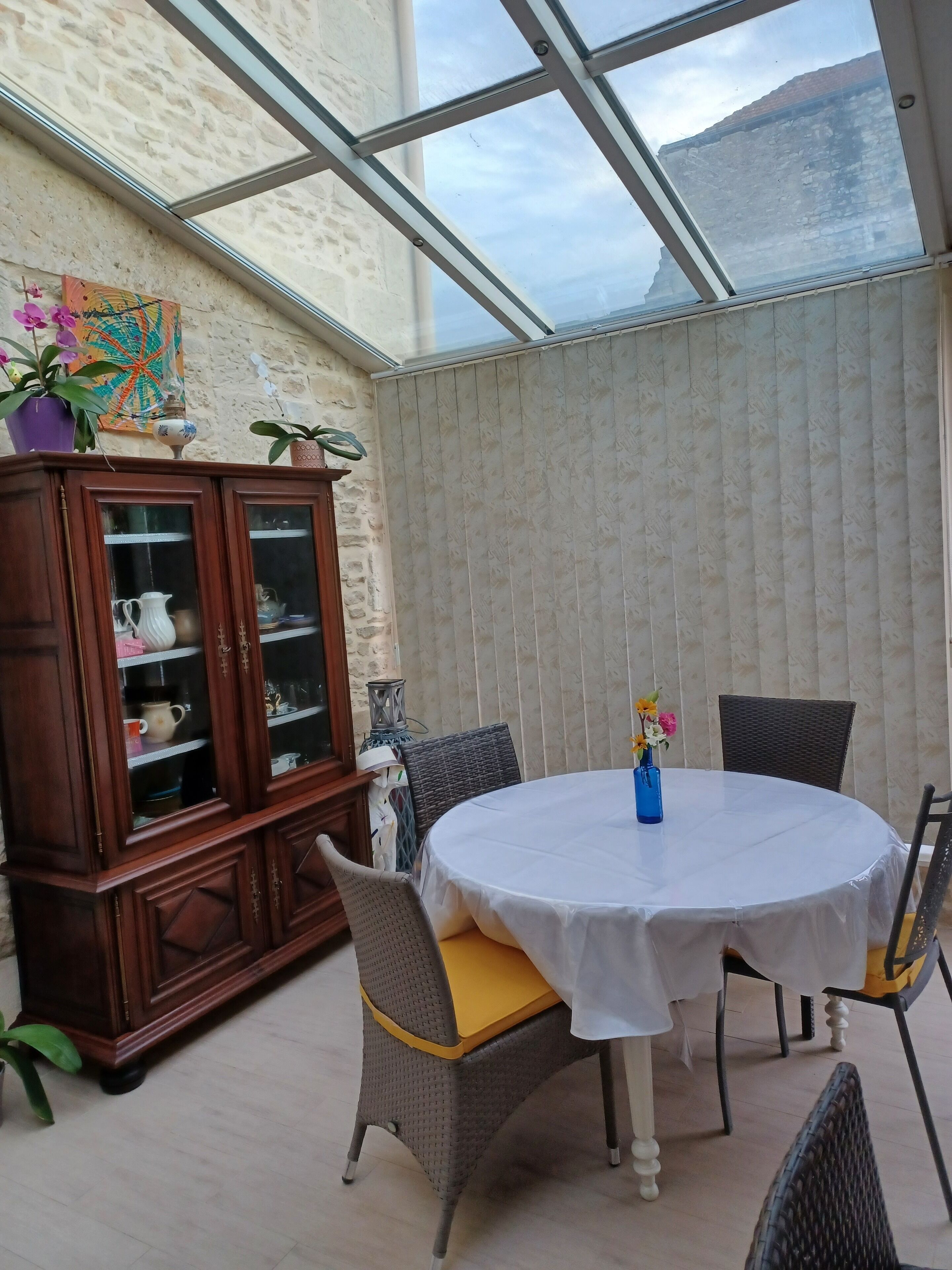 Een oranjerie met een ronde tafel, rieten stoelen en een houten kast met glazen deuren.