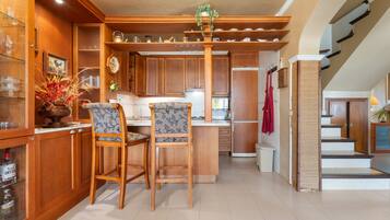 Una cocina con armarios de madera, una isla central, dos taburetes de bar y una planta colgante.