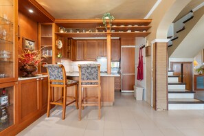 A kitchen with wooden cabinets, a central island, two bar stools, and a hanging plant.