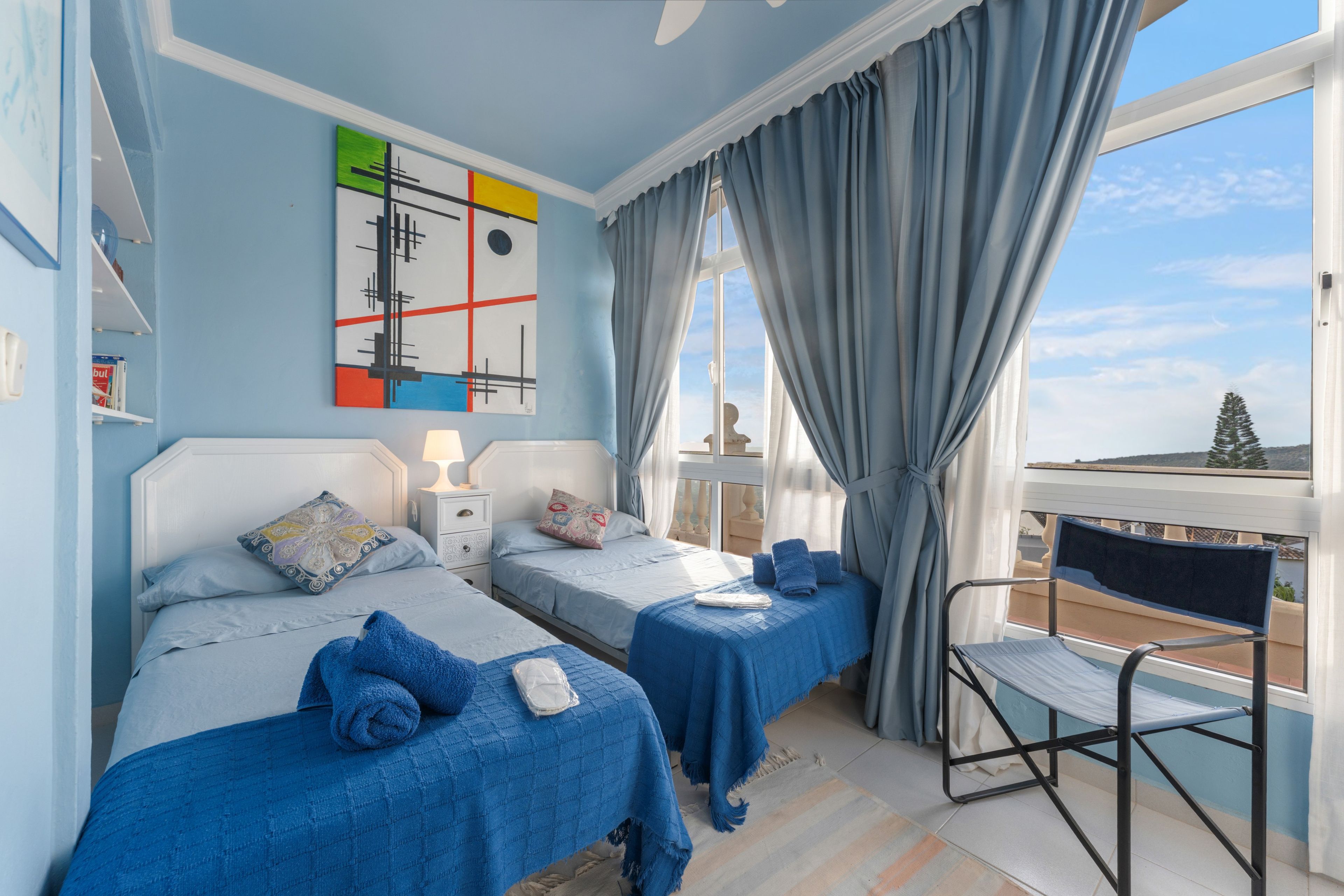 Une chambre d’hôtel avec deux lits, une fenêtre avec des rideaux, un tableau au mur et une vue sur l’extérieur.