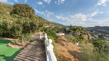 Un sendero lleva a una ladera con baranda blanca, rodeada de vegetación y con vistas a un pueblo.