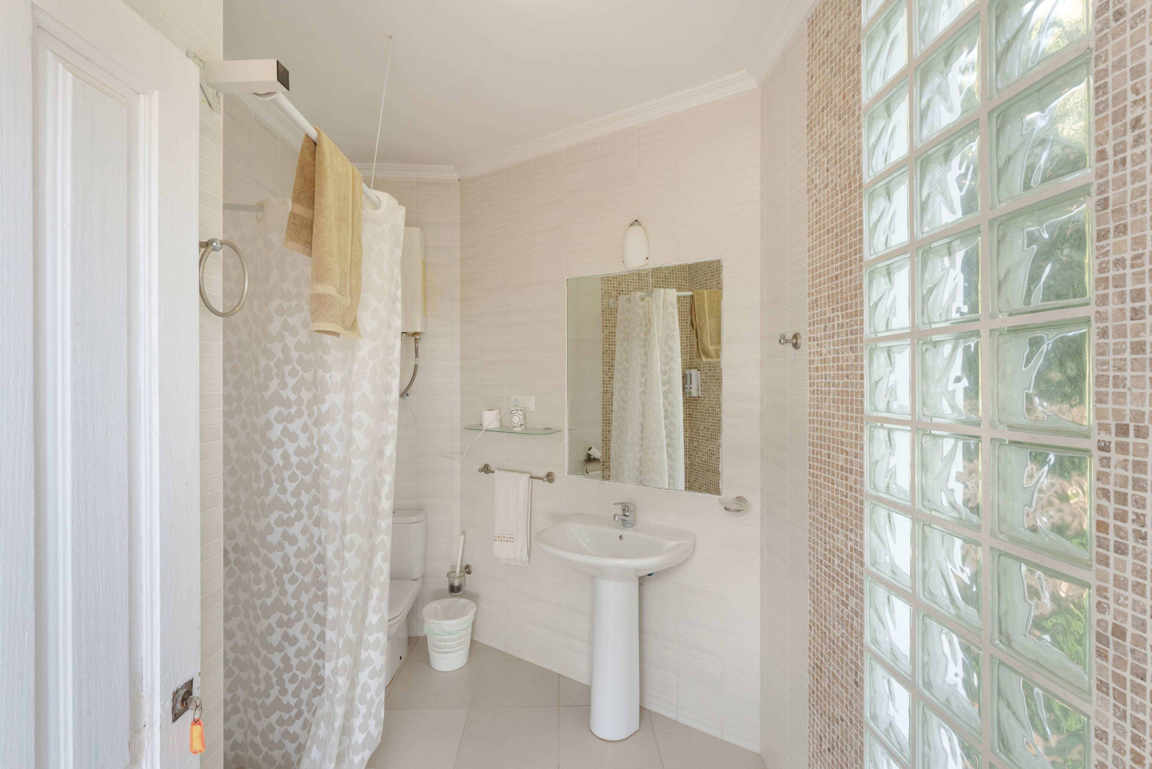Un baño con ducha, inodoro, lavamanos y un ventanal con diseño de celosía.