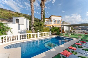Une piscine entourée d’une clôture blanche, avec des chaises longues et un bâtiment doté d’un balcon.