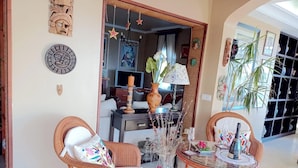Ein Zimmer mit Korbmöbeln, einem Glastisch, einer Blumenvase und Wanddekorationen.