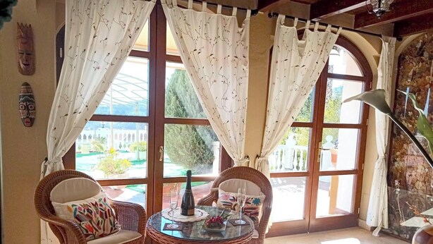 Ein Zimmer mit großen Fenstern, Korbmöbeln und einer Champagnerflasche auf einem Tisch.