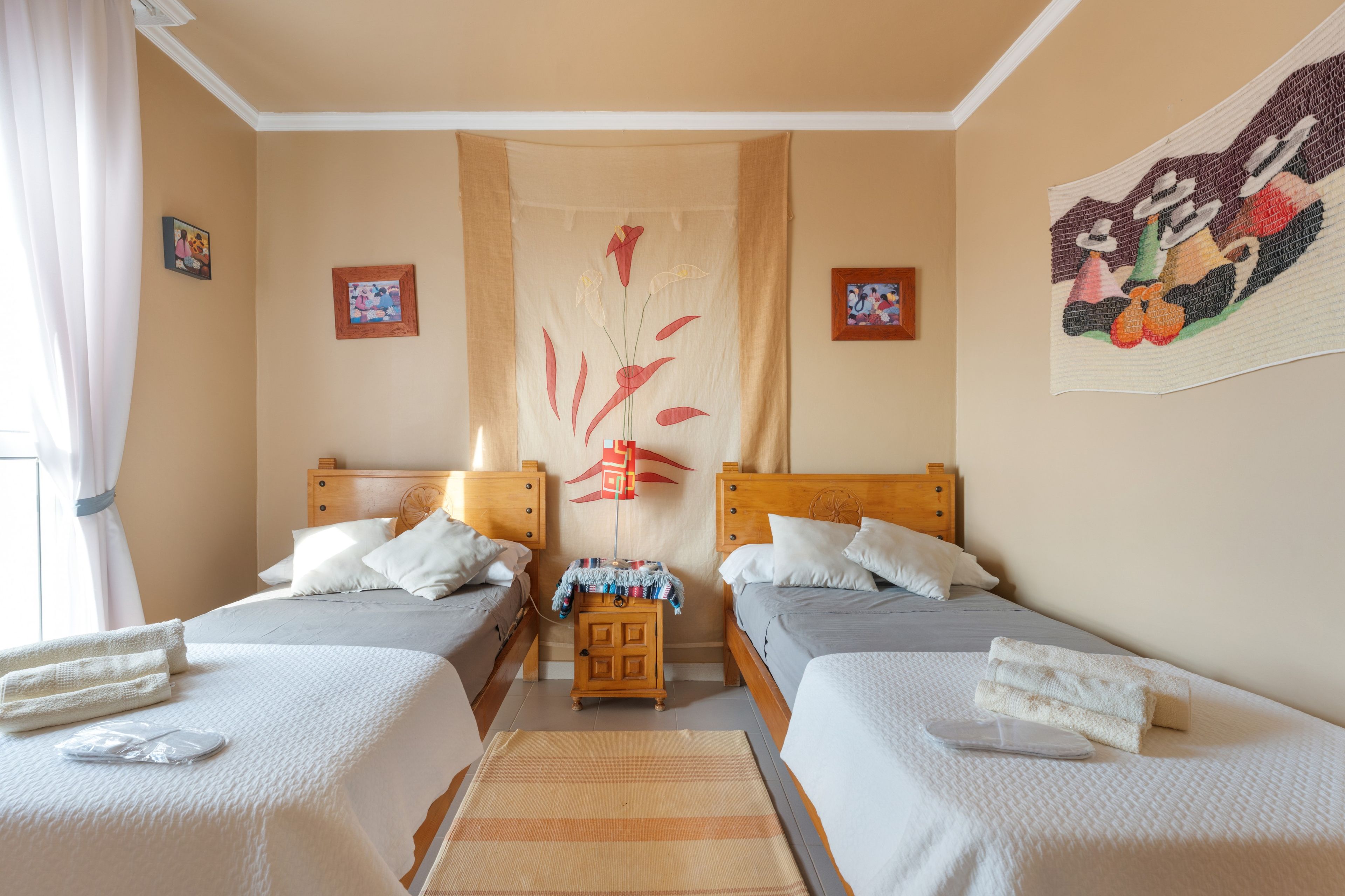 Ein Hotelzimmer mit zwei Betten, einem Holz-Kopfteil, einem kleinen Tisch und einer Wandweberei.