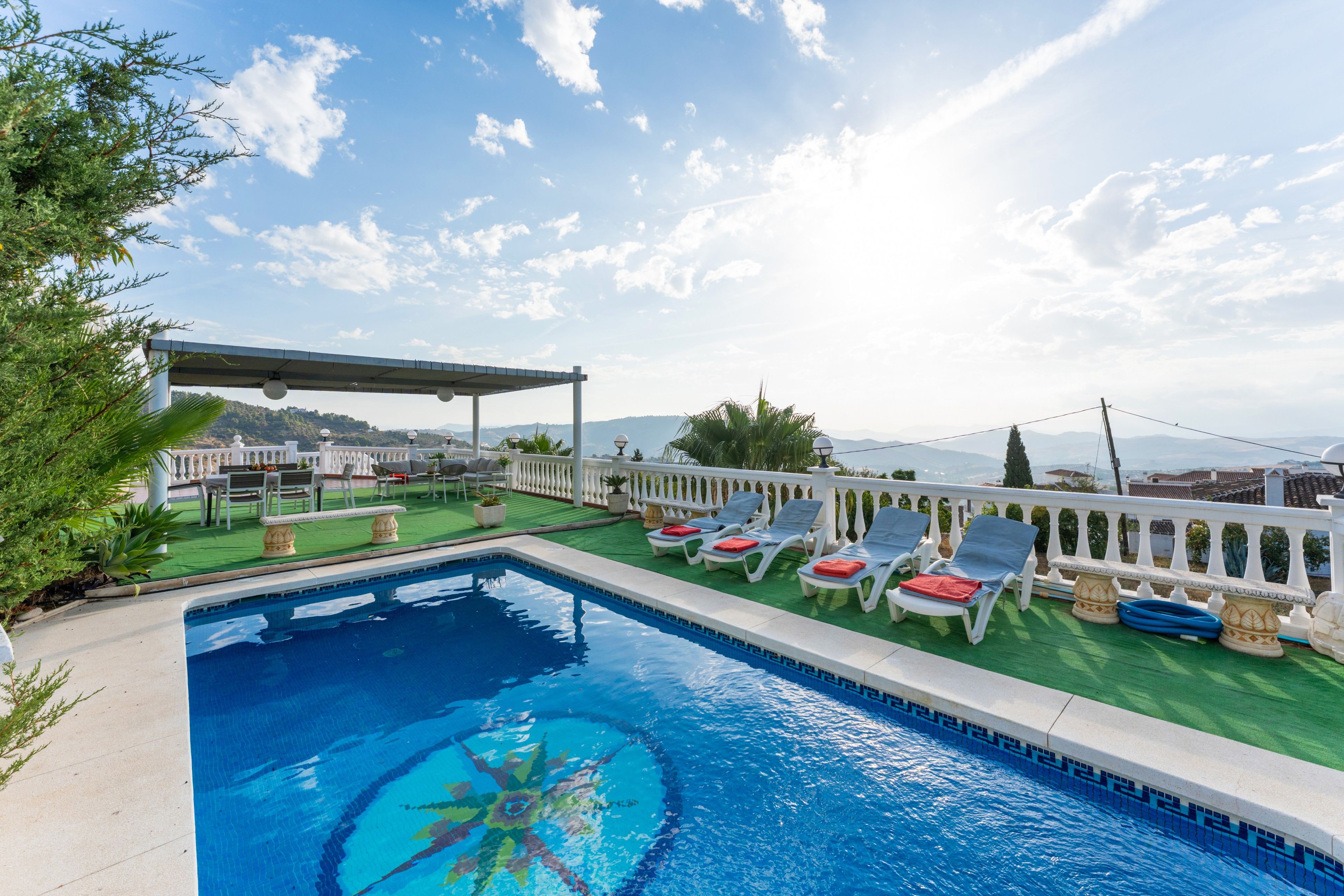 Una piscina con sillas de descanso y un pérgola, rodeada de vegetación y con vistas a un paisaje pintoresco.