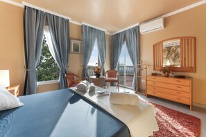 A hotel room with a bed, a chair, a dresser, and a balcony with a view.