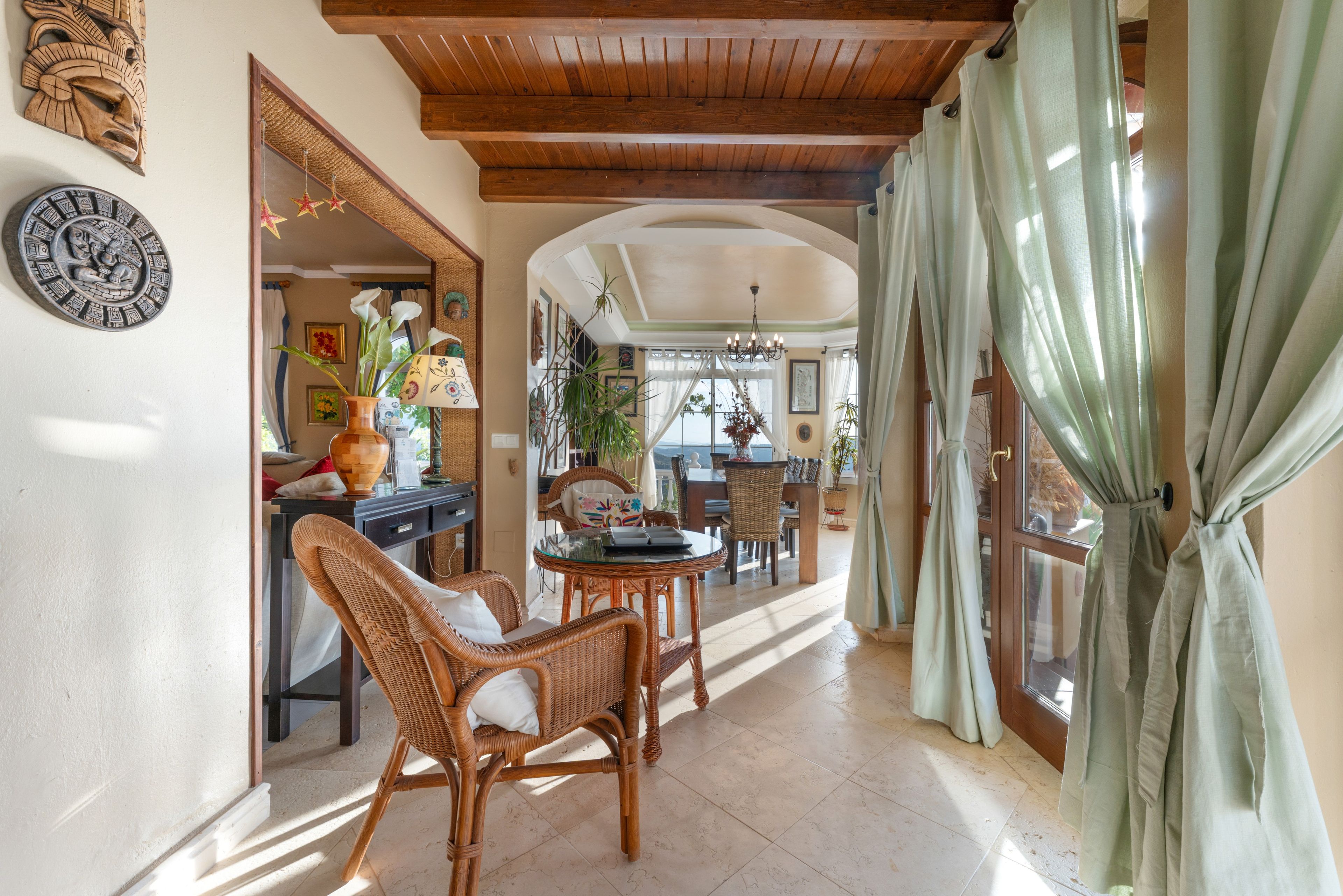 Una habitación amplia con techo alto, muebles de mimbre y vistas por un gran ventanal.