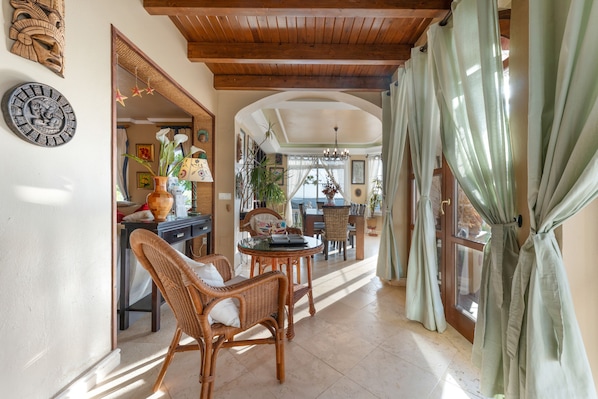 A spacious room with a high ceiling, wicker furniture, and a view through a large window.