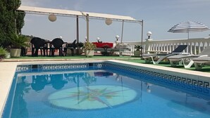 Ein Poolbereich mit Liegestühlen, Sonnenschirmen und einer Pergola.