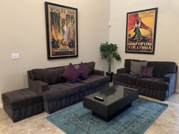 A living room with two dark sofas, a glass coffee table, and a large potted plant.