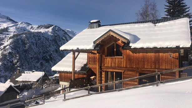 Eine Holzhütte mit schneebedecktem Dach vor einer Bergkulisse.