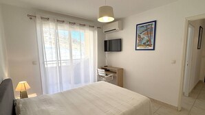 Un dormitori amb un llit, una taula de treball, una cadira, un televisor i un quadre a la paret.