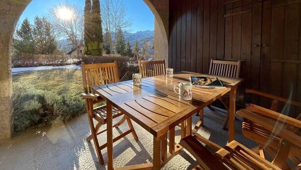 Un tavolo e delle sedie di legno in uno spazio parzialmente aperto, con vista su alberi e montagne.