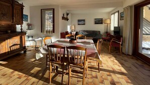 Zona pranzo con tavolo apparecchiato per quattro, circondato da sedie in legno. Sullo sfondo, un divano e una televisione.