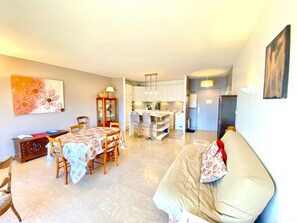Sala de estar com sofá, mesa de jantar e cadeiras, cozinha ao fundo e um quadro na parede.
