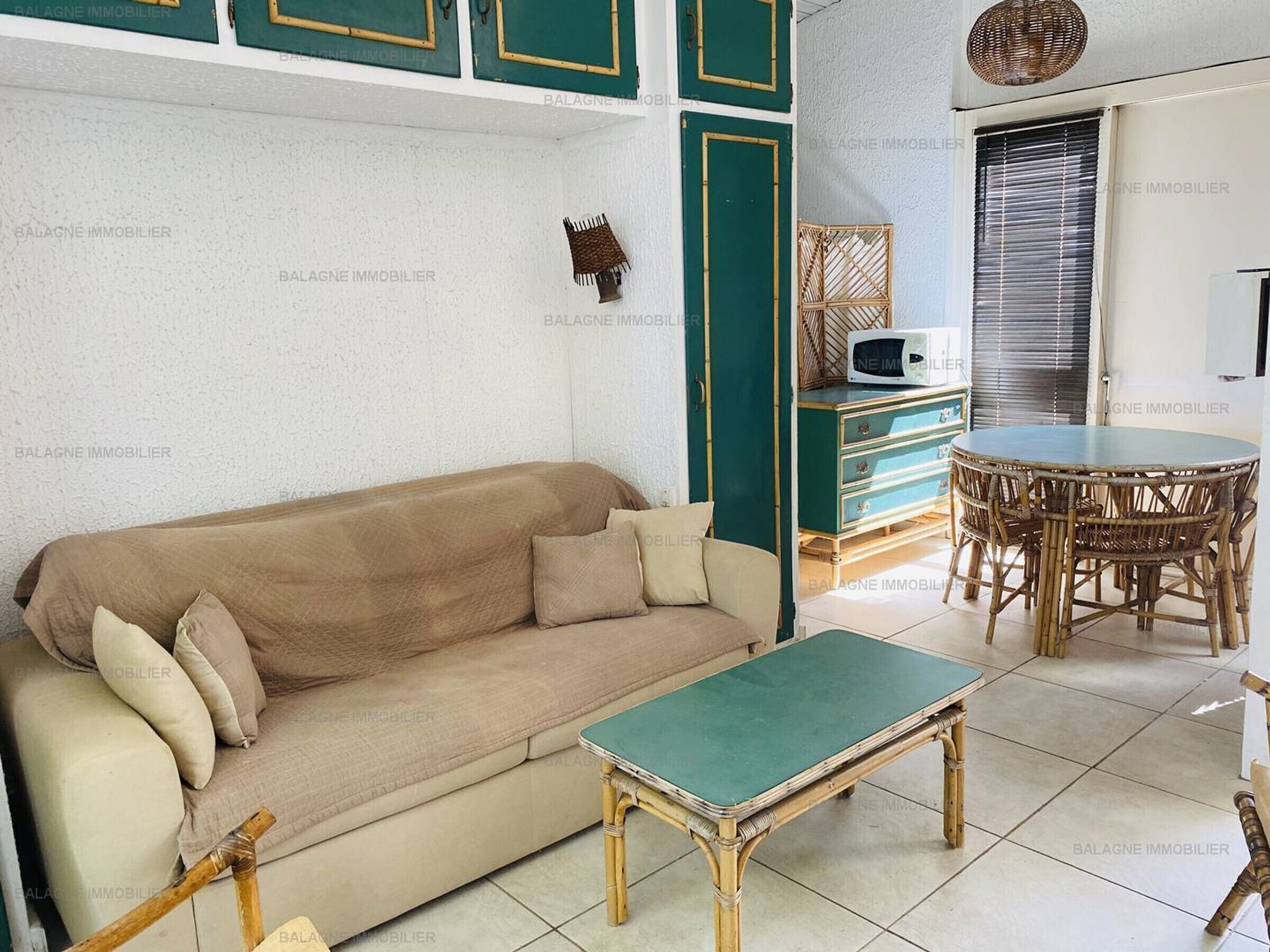 A living room with a beige sofa, a green coffee table, wicker furniture, and a microwave on a cabinet.