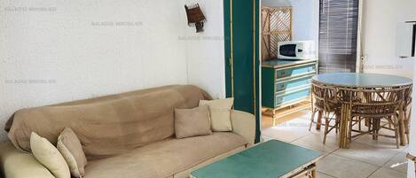 A living room with a beige sofa, a green coffee table, wicker furniture, and a microwave on a cabinet.