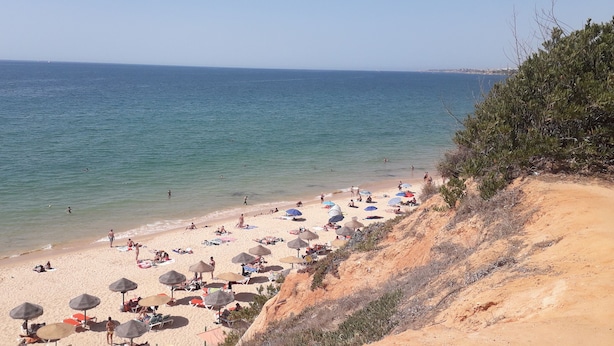 En strand med parasoller og liggestole, sand og hav i baggrunden.