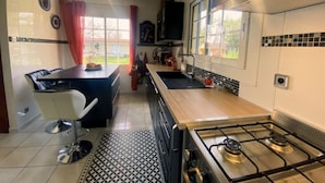 Et moderne køkken med gaskomfur, et spiseområde med en hvid stol og et vindue med gardiner.