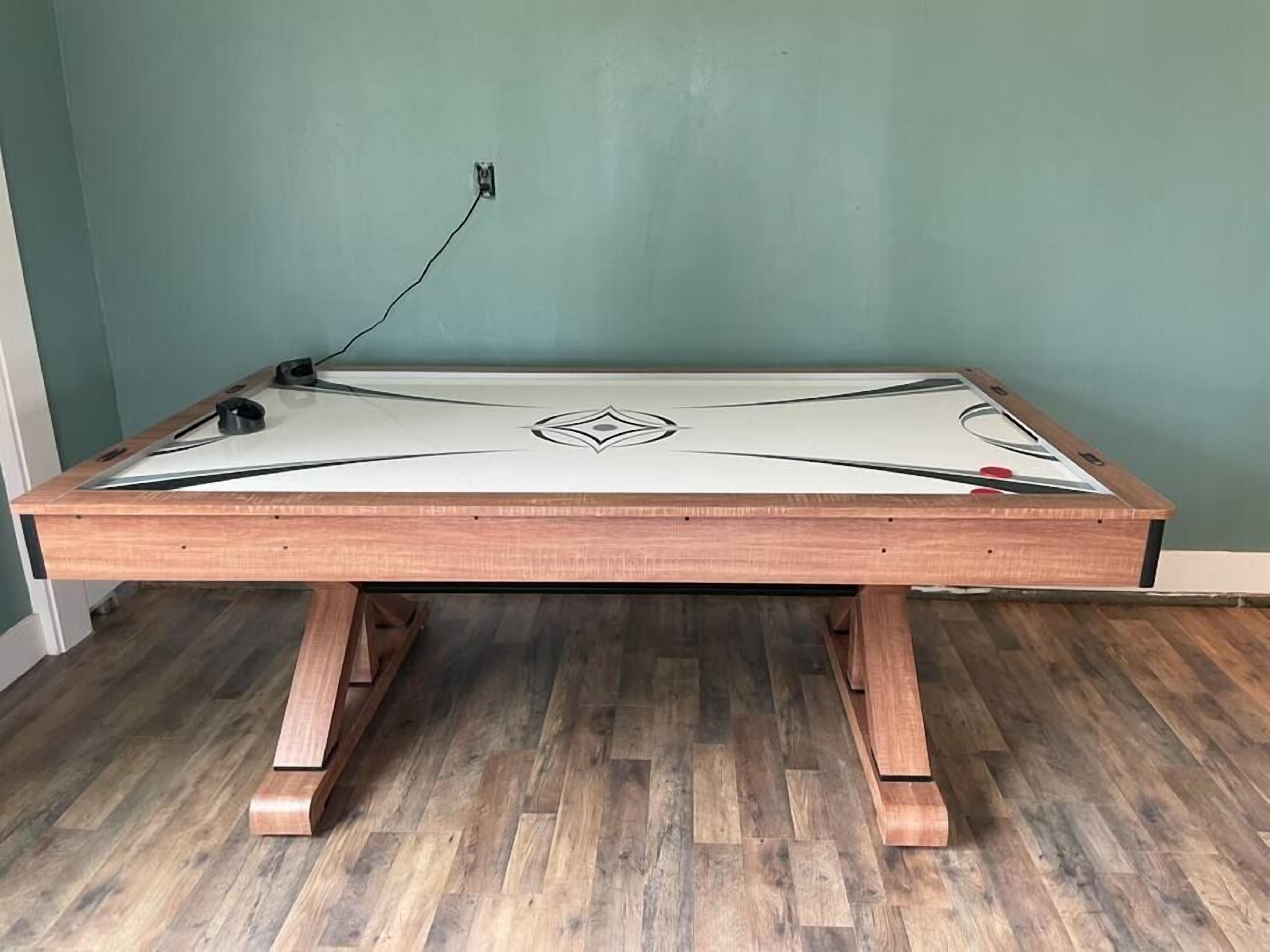 Une table de billard avec un cadre en bois et un plateau de jeu blanc, placée contre un mur de couleur turquoise.