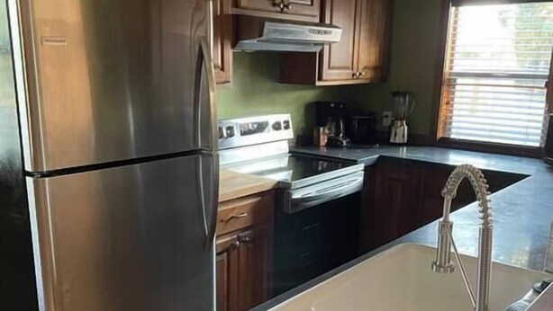 A kitchen with a stainless steel refrigerator, wooden cabinets, a black countertop, and a sink with a modern faucet. - CUTE COTTAGE WITH A GAME ROOM (Belgrade)