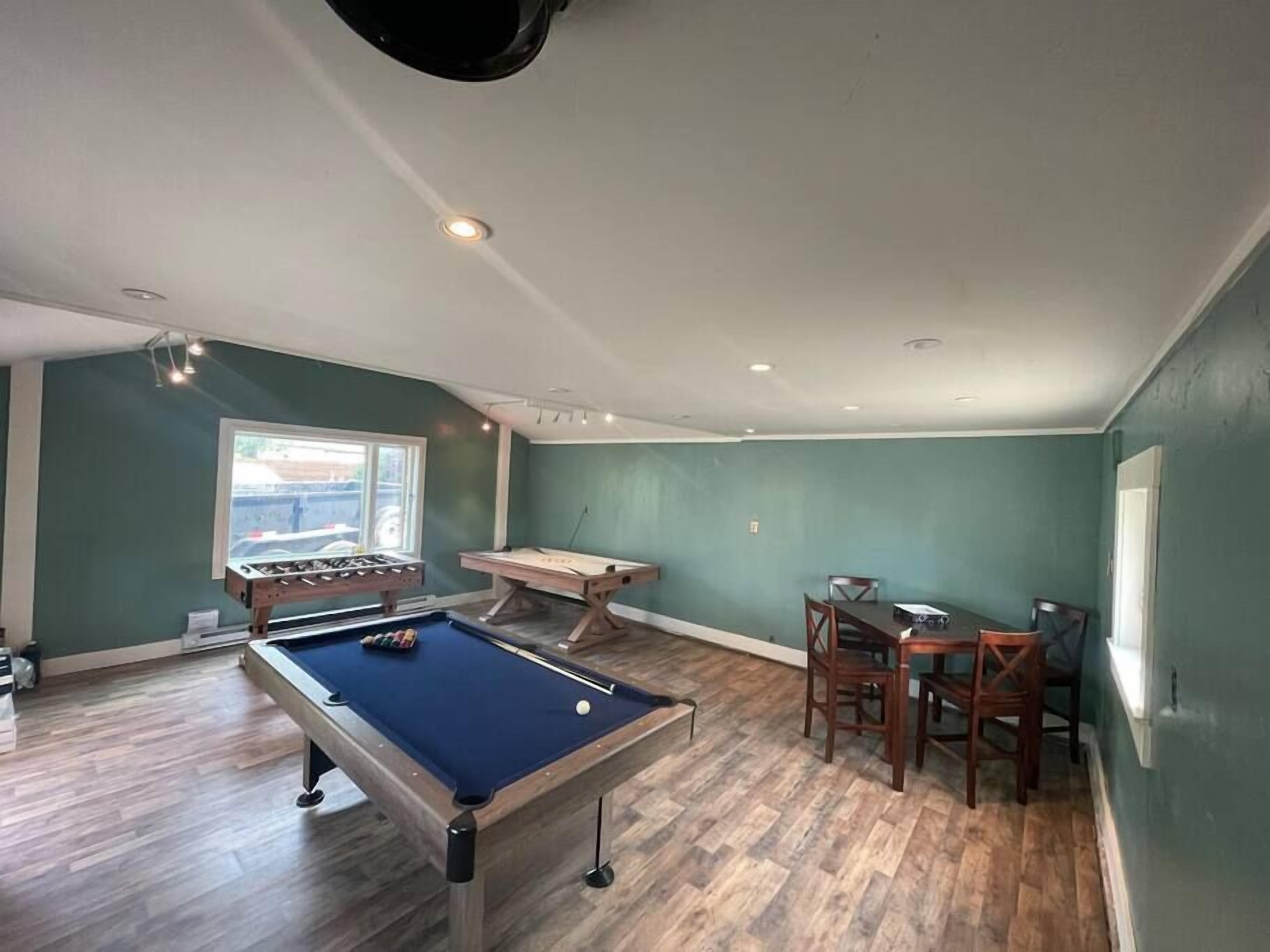 A pool table, foosball table, and a dining area with chairs and a table in a room with green walls and wooden flooring.