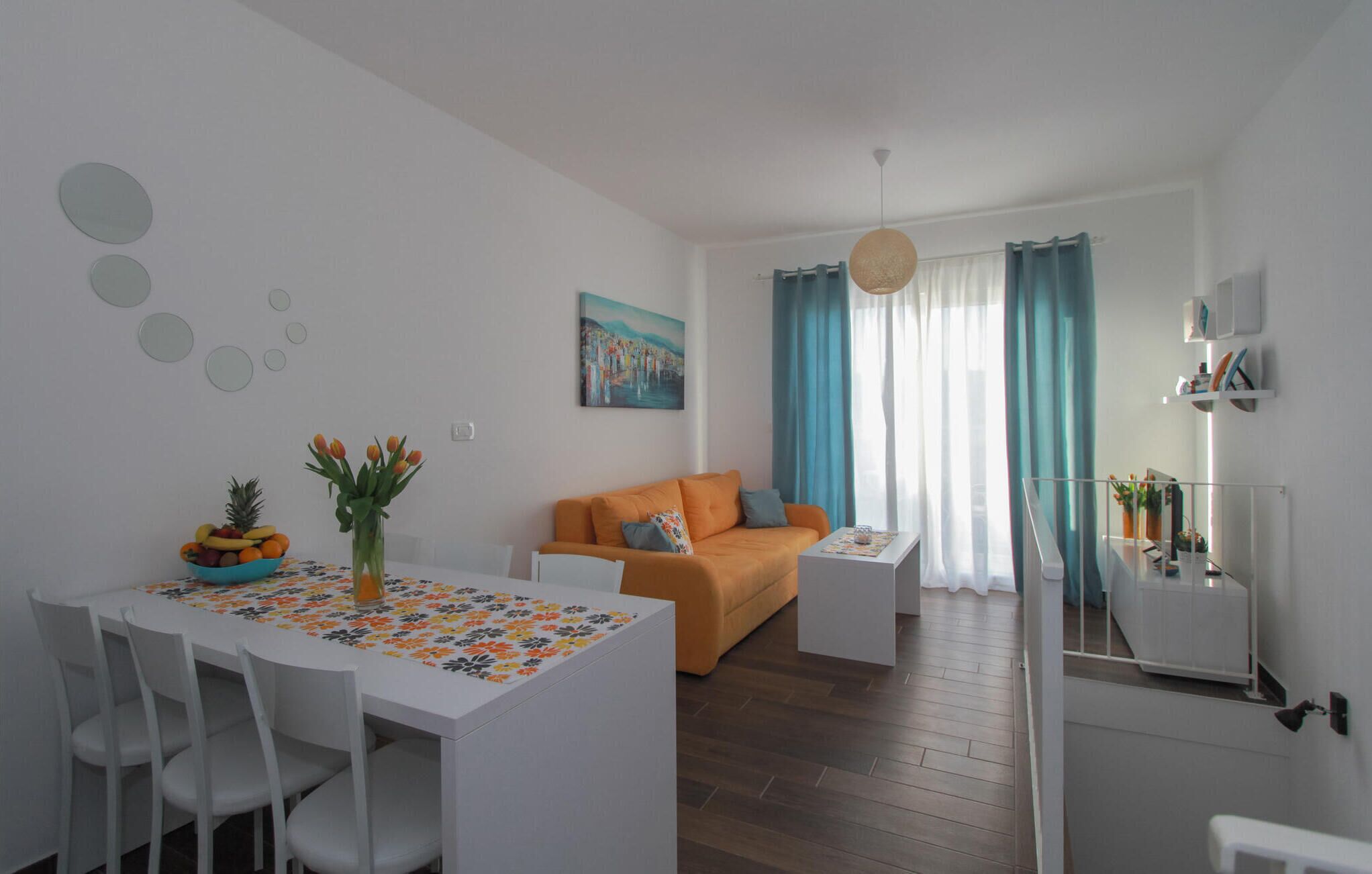 A modern living room with a white dining table, orange sofa, and a painting on the wall.