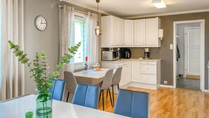 A modern kitchen with white cabinets, a dining table with blue chairs, and a clock on the wall.
