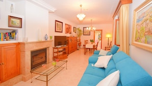 A living room with a fireplace, blue sofa, dining area, and a chandelier. - Can Nina 198 traditional finca with private swimming pool, terrace, barbecue and WiFi (Campanet)