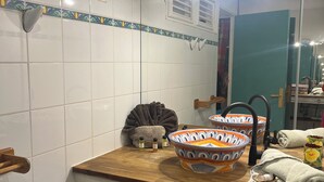 Un baño con paredes de azulejos blancos, un mueble de tocador de madera, un espejo grande y un lavabo con grifo.