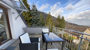 Ein Balkon mit Korbmöbeln, einer Glastür und Blick auf ein bewaldetes Gebiet.