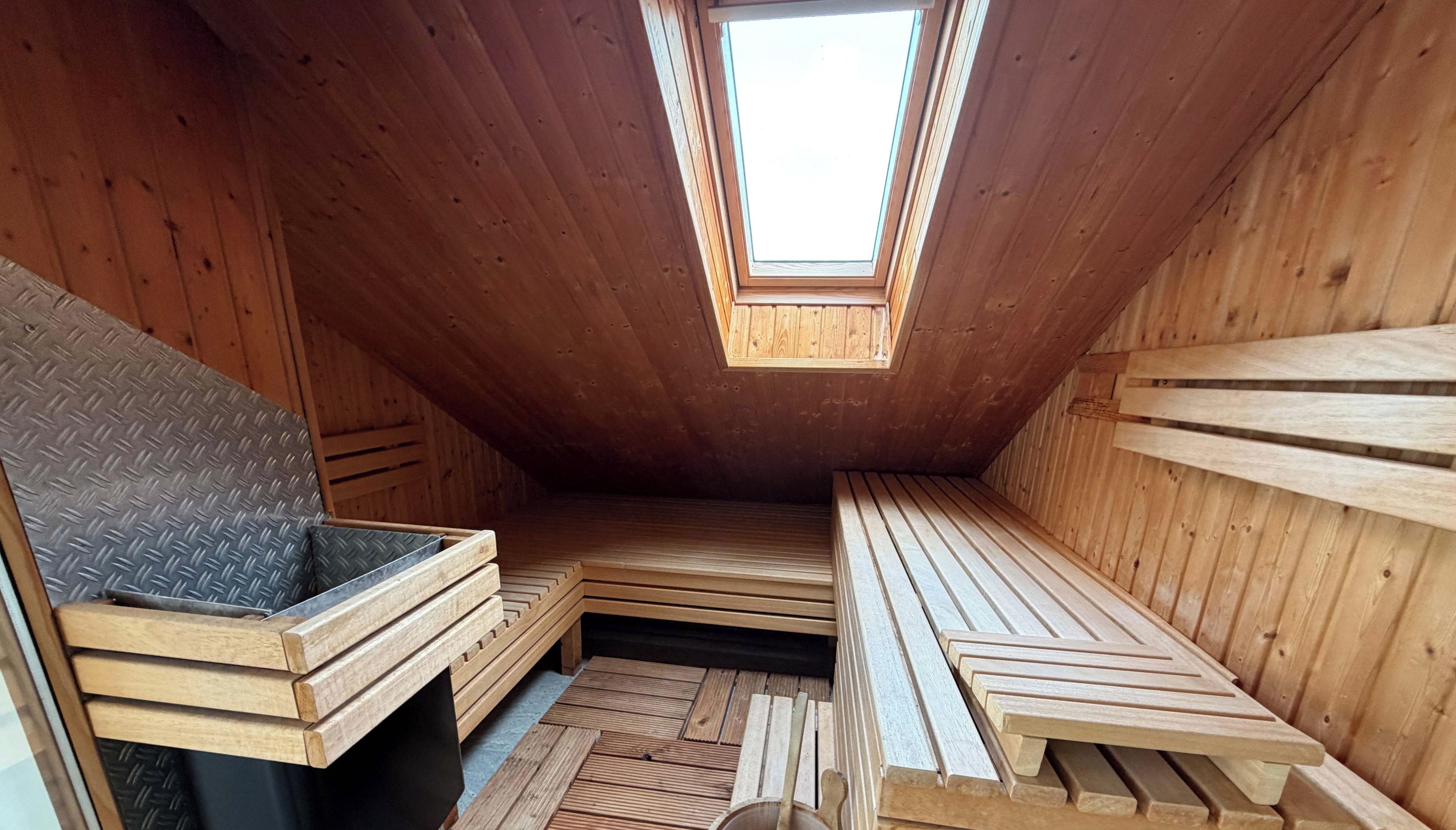 Een kleine zolderkamer met een schuine plafond, houten wanden en een dakraam.