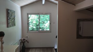 A room with a sloped ceiling, a large window with a view of greenery, a vase with flowers, and a painting on the wall. - Guest house ideally located (La Teste-de-Buch)