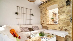 Un salon chaleureux avec un canapé blanc, des fauteuils en osier, une table basse en verre et un mur en pierre.