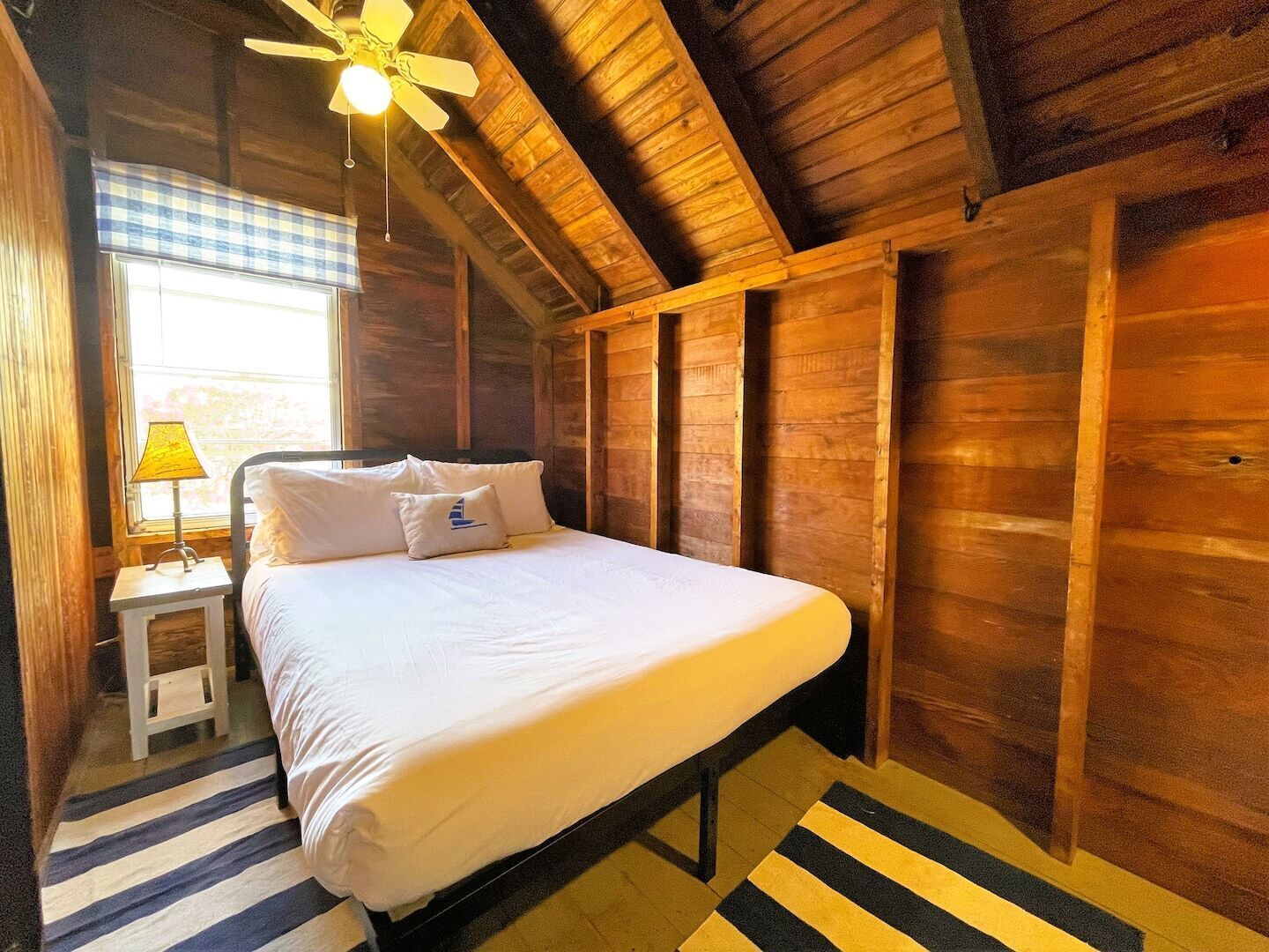 A bedroom with a bed, a nightstand, a lamp, and a window with blinds.