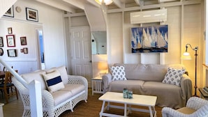 A cozy living room with wicker furniture, a painting of sailboats, and a ceiling fan.