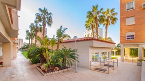 A courtyard with palm trees, a tiled floor, and a building with a red-tiled roof. - Cozy apartment in Alicante (Alacant) with sauna (Alicante (Alacant))