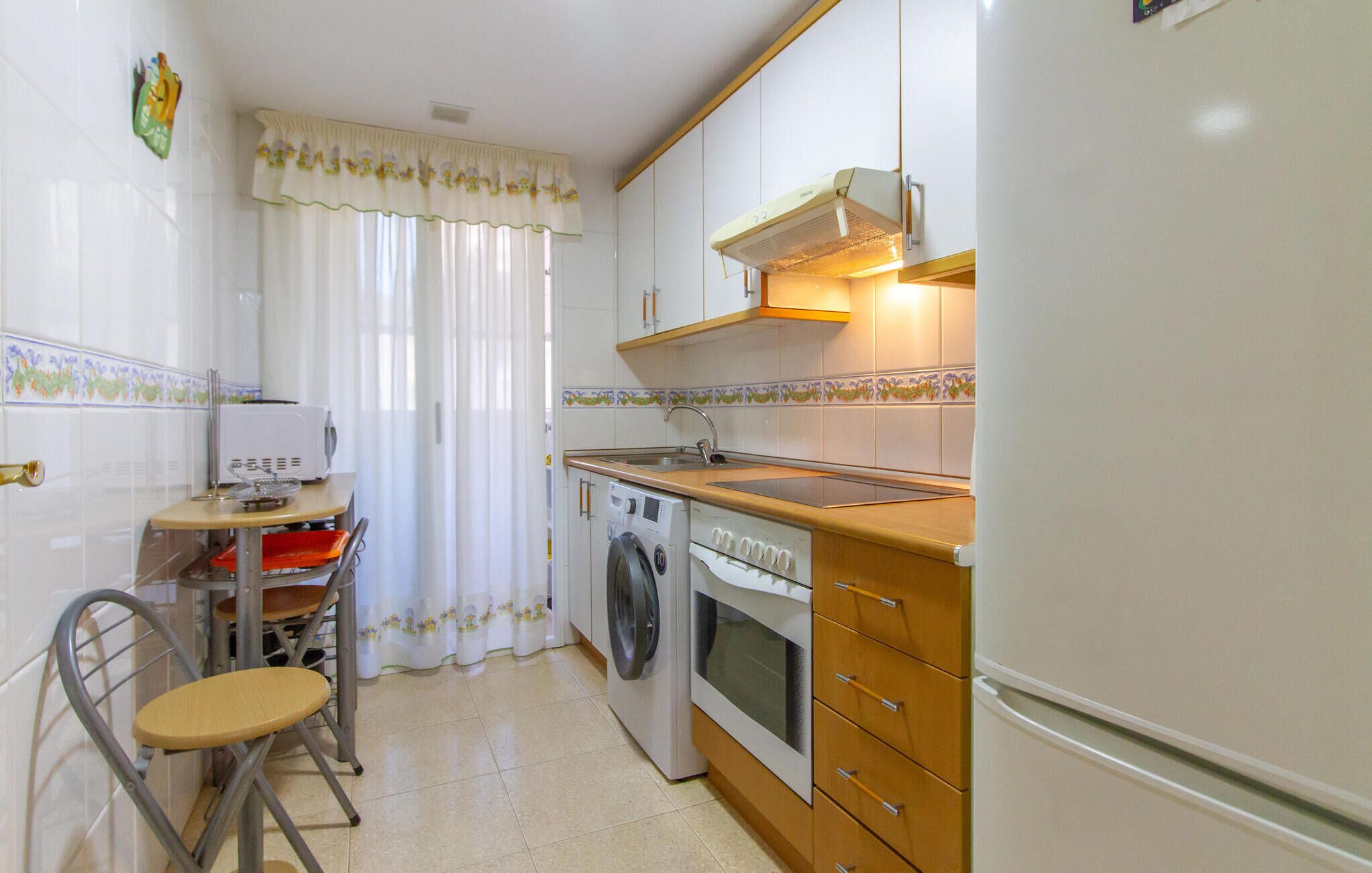 A compact kitchen with a washing machine, oven, and a small table with a chair.