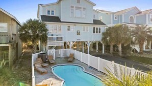 Une grande maison avec une piscine, des balustrades blanches et des palmiers.