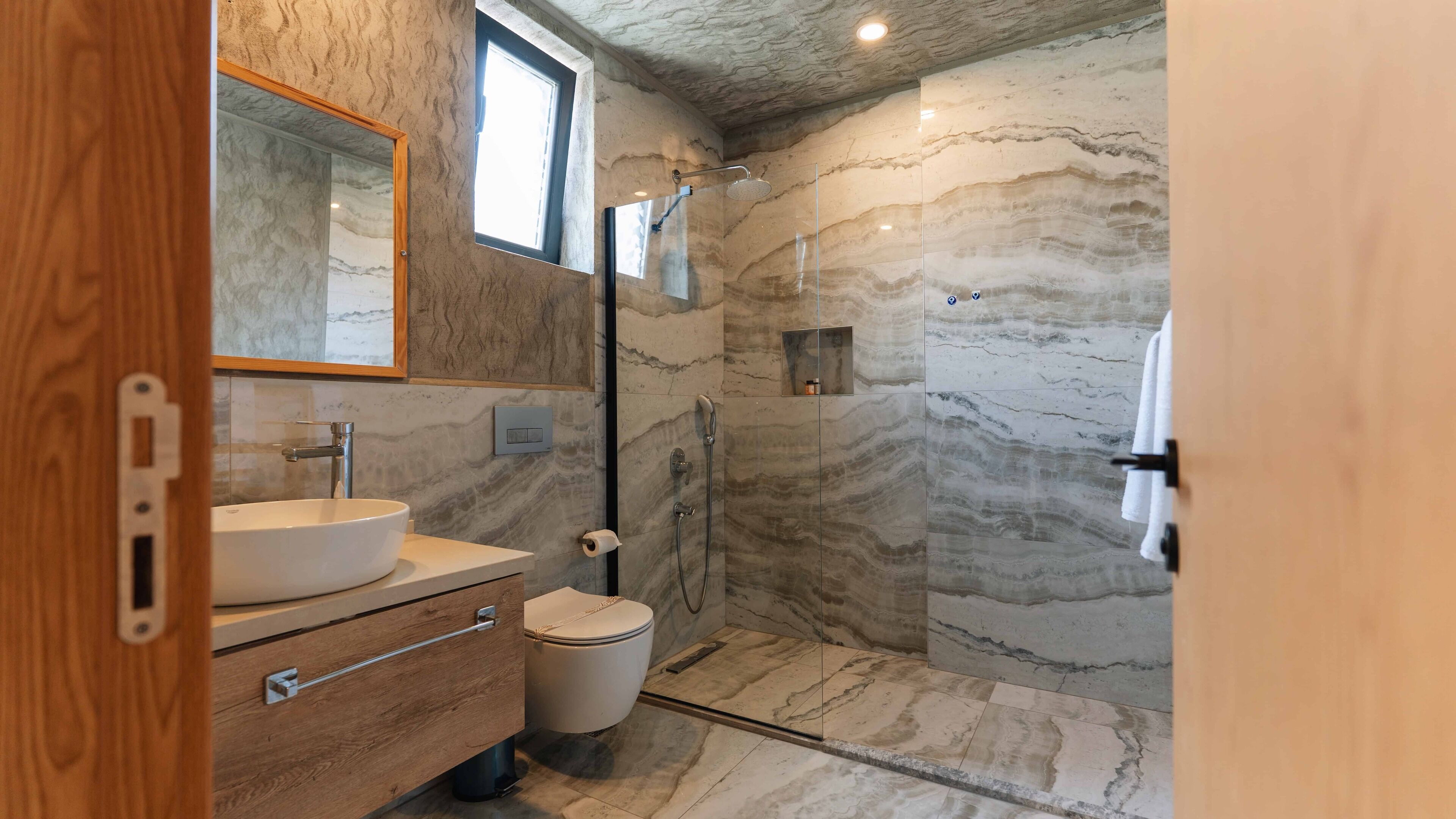 A modern bathroom with a marble vanity, a glass shower enclosure, and a wooden cabinet.