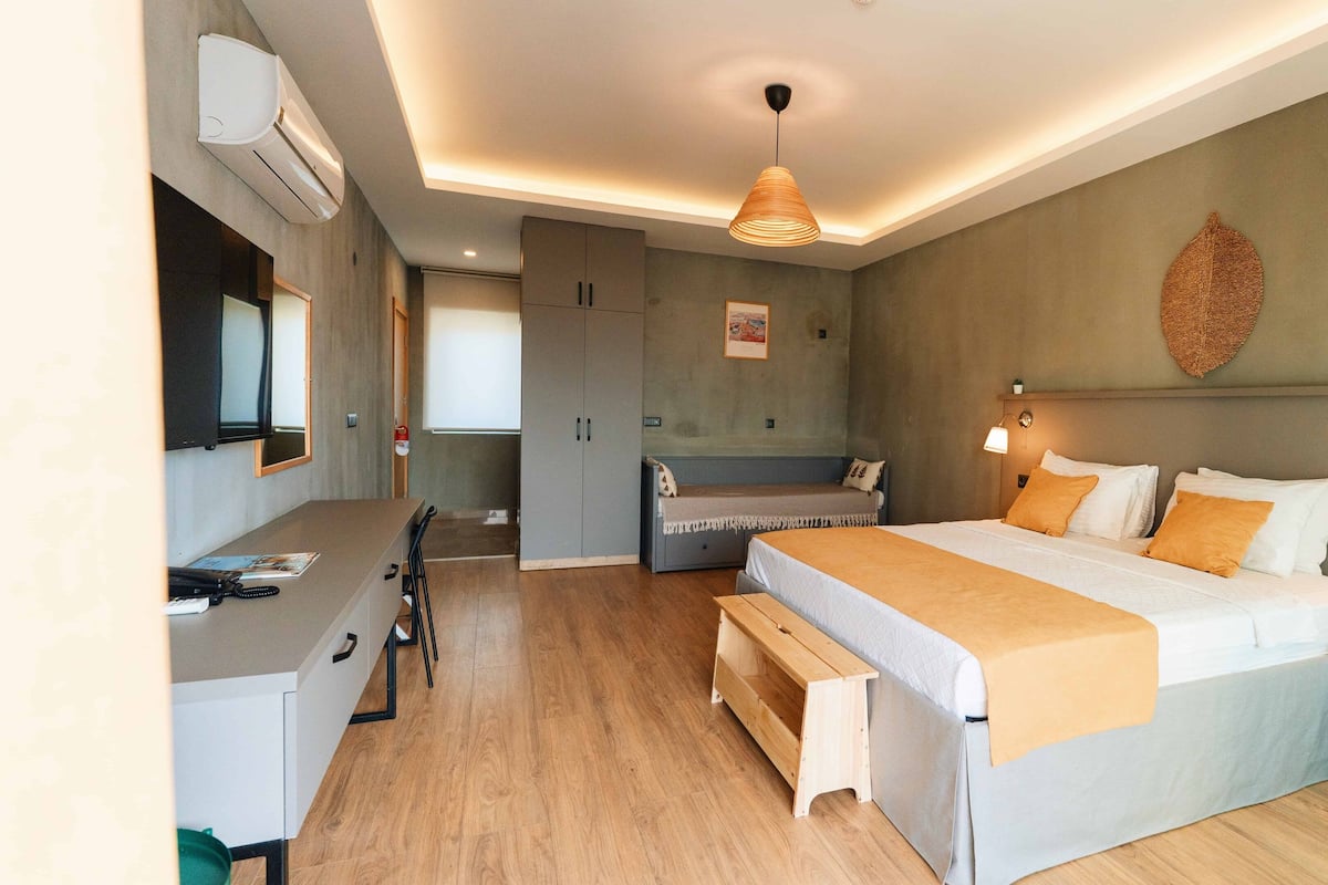 A modern hotel room with a bed, bedside table, desk, and wardrobe.
