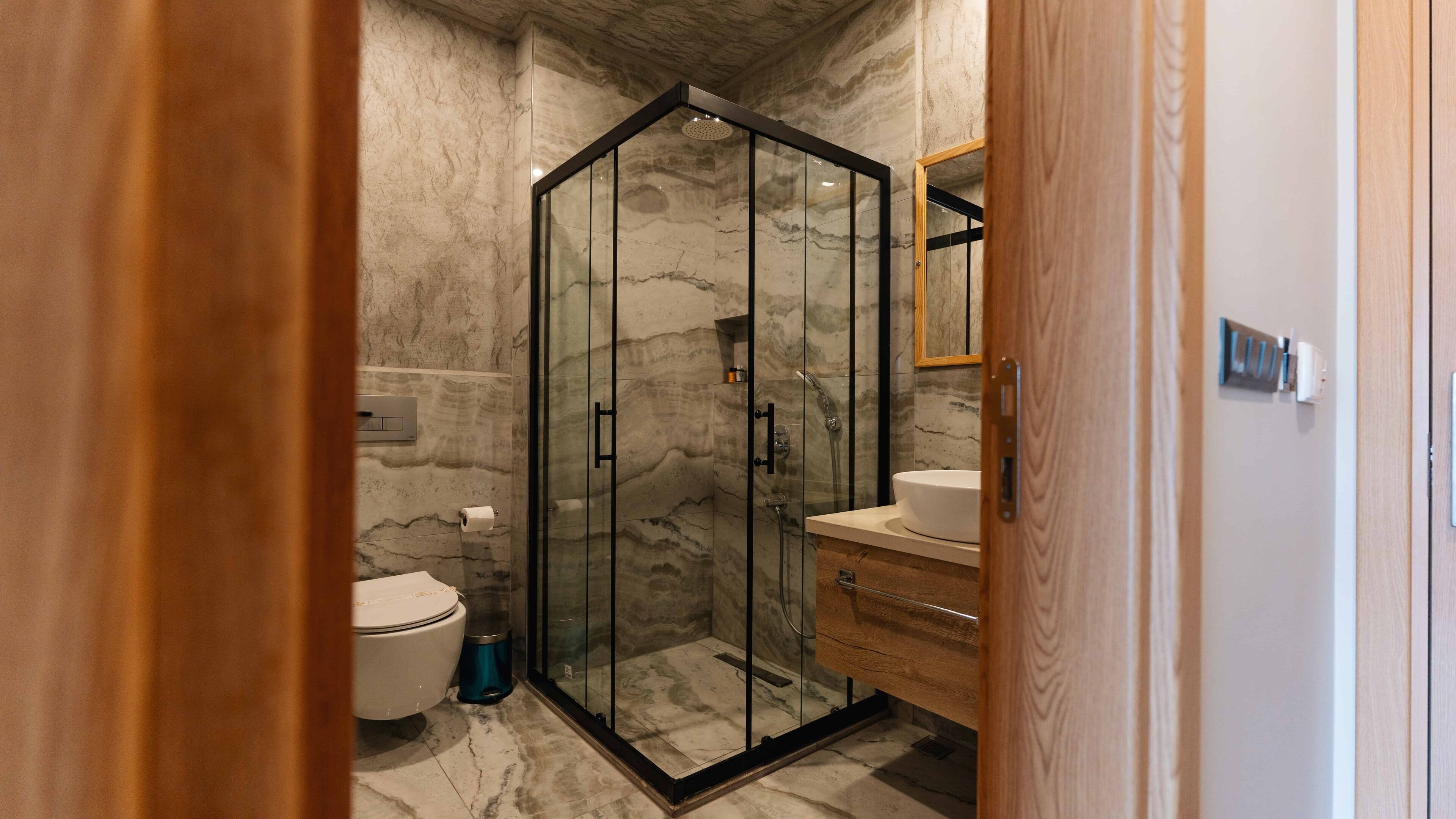 Un baño moderno con ducha de vidrio, paredes de mármol, inodoro y tocador de madera.