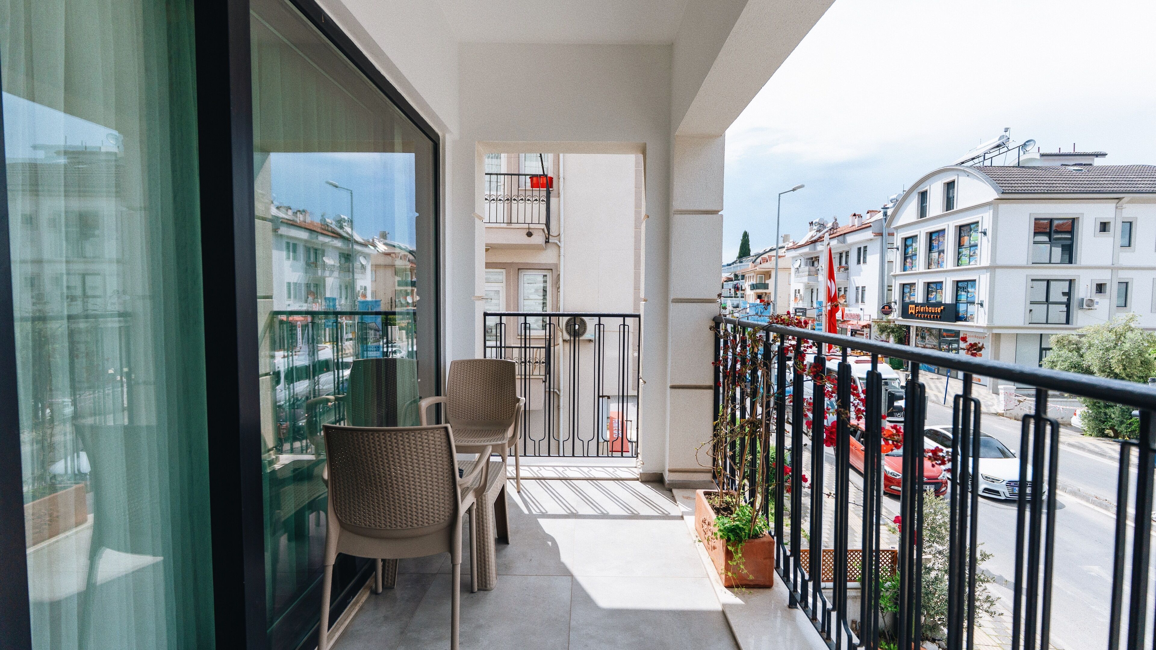 Ein Balkon mit zwei Korbstühlen, einem Blumentopf und Blick auf die Straße und die Häuser.