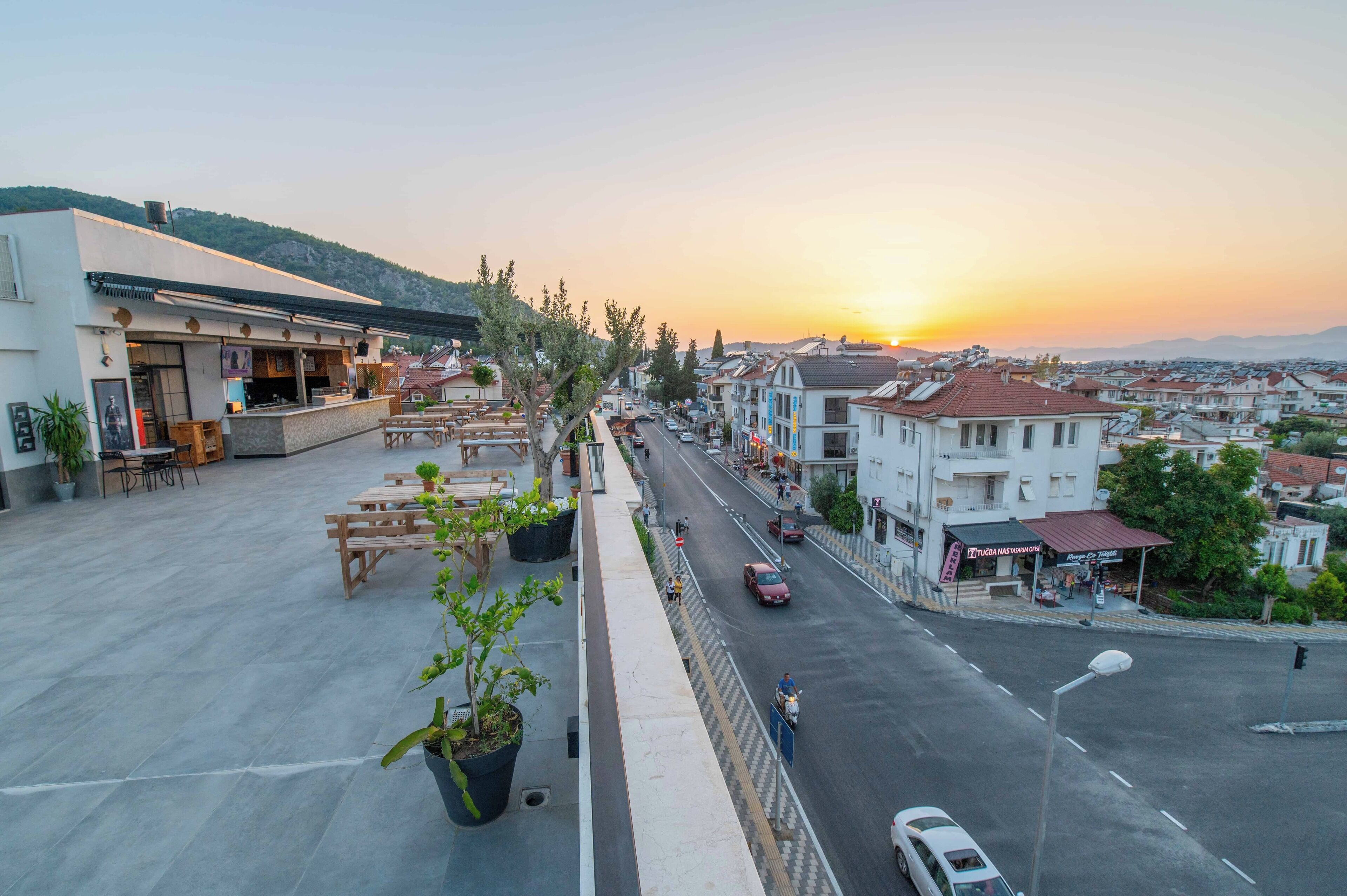 A terrace with outdoor seating, a view of the street, and a sunset.