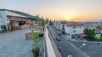 A terrace with outdoor seating, a view of the street, and a sunset.