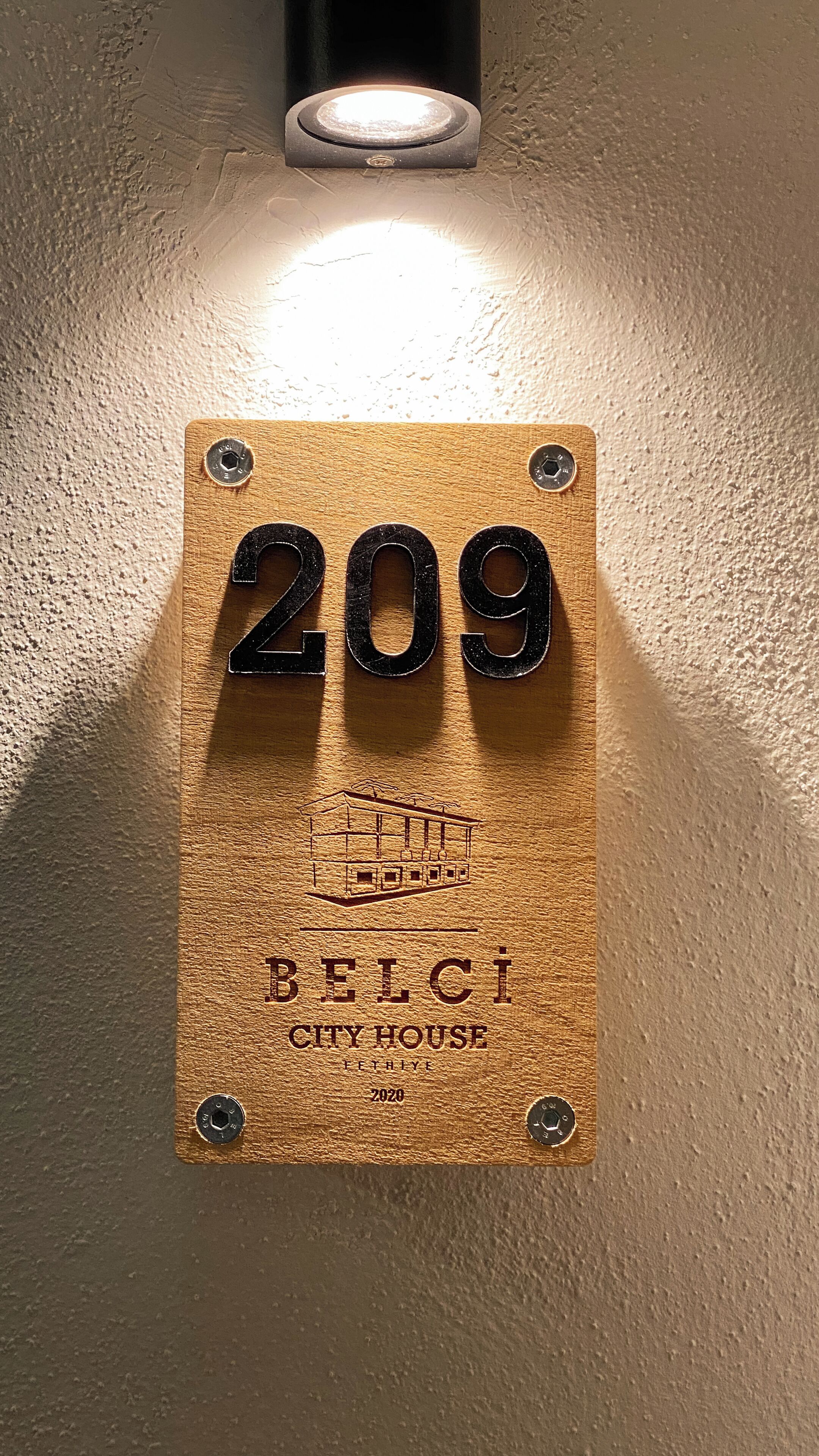 A wooden plaque with the number 209 and the text "BELCI CITY HOUSE" on a textured wall.